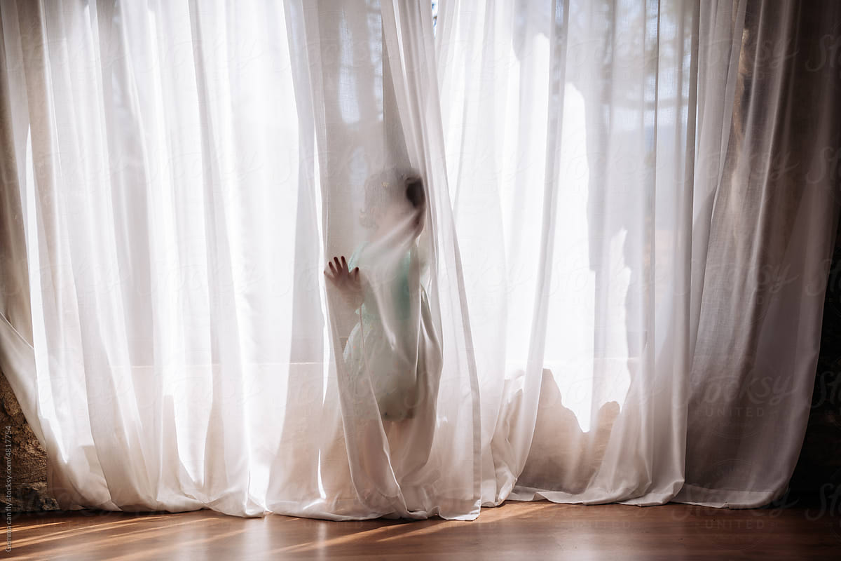 Little girl playing hidden behind curtains