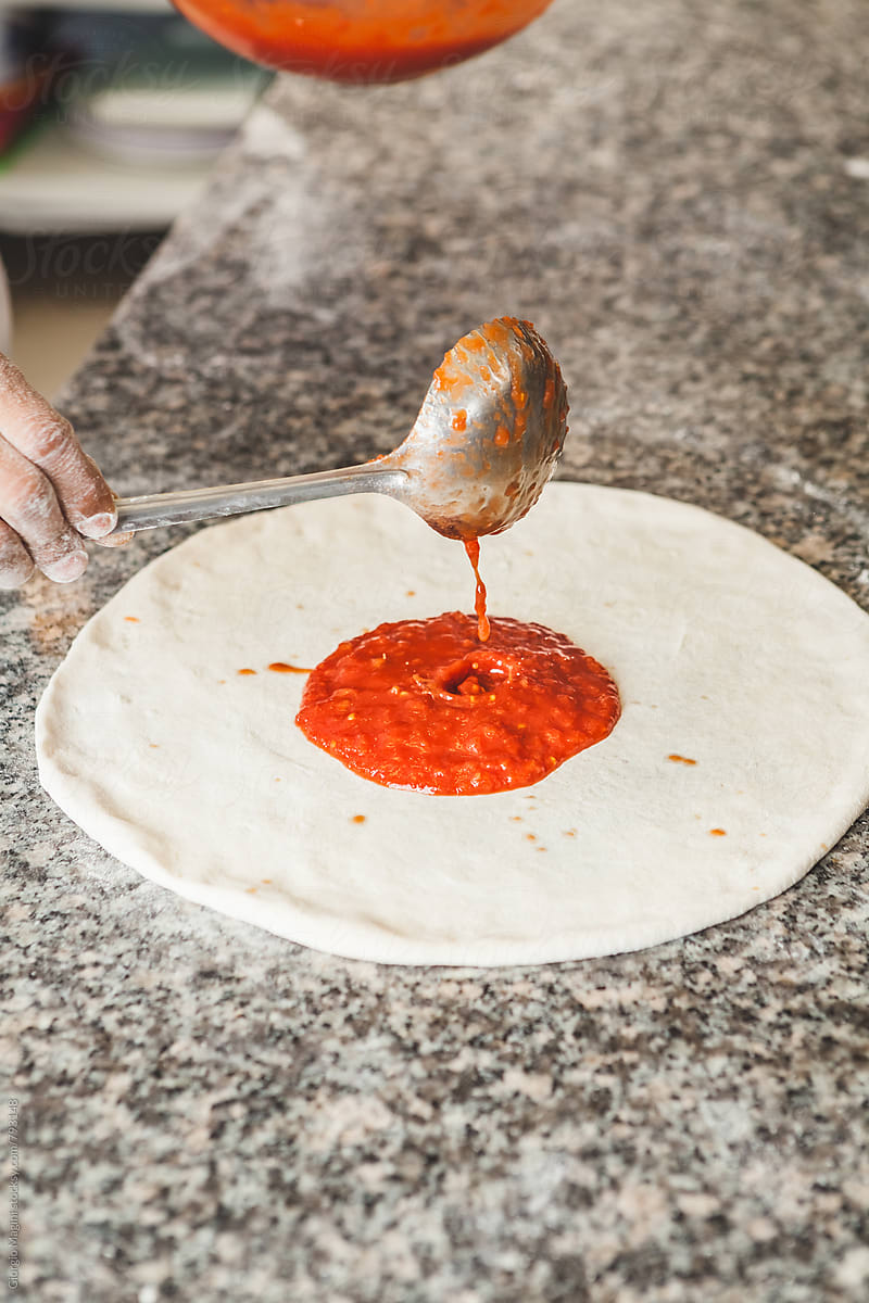 Pouring Tomato Sauce on the Raw Dough of a Pizza