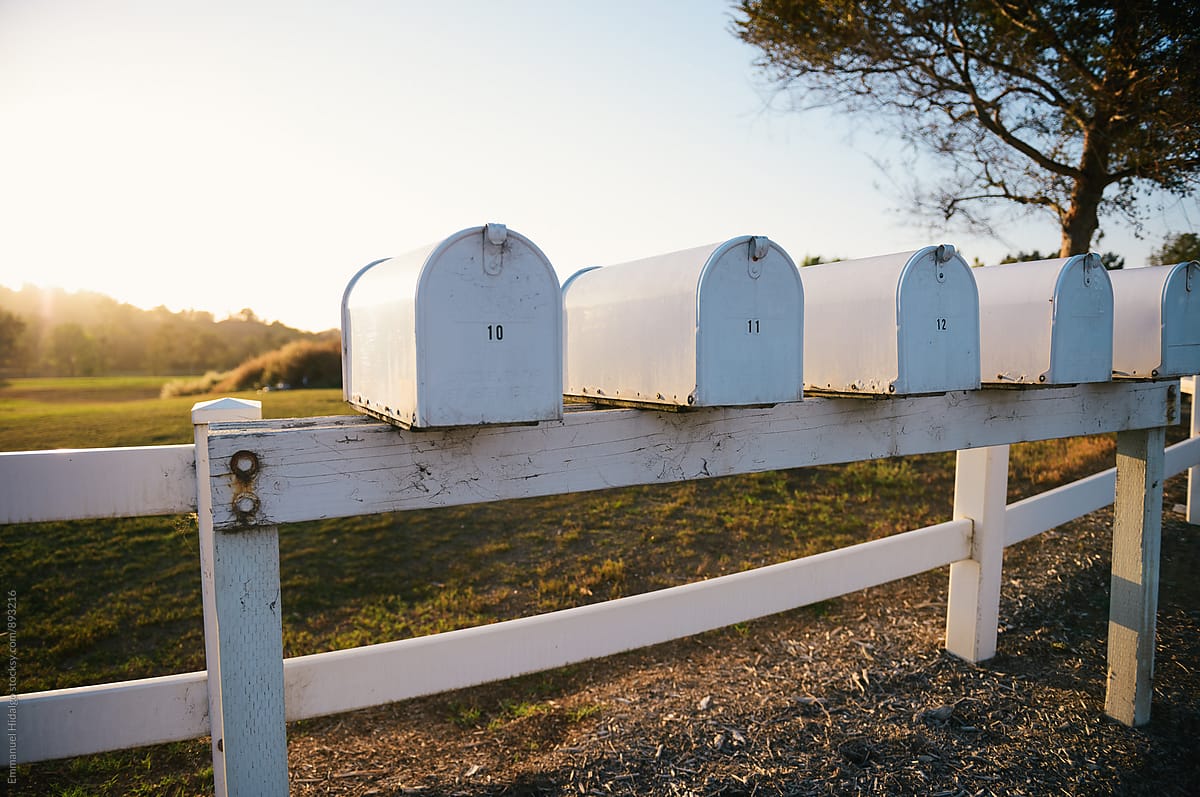 Multiple white mailboxes line a wooden fence