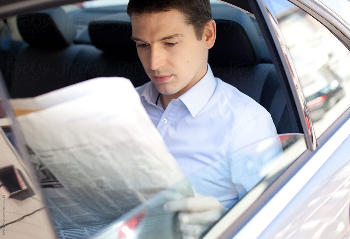 Businessman sitting in a backseat of the car and reading newspapers.