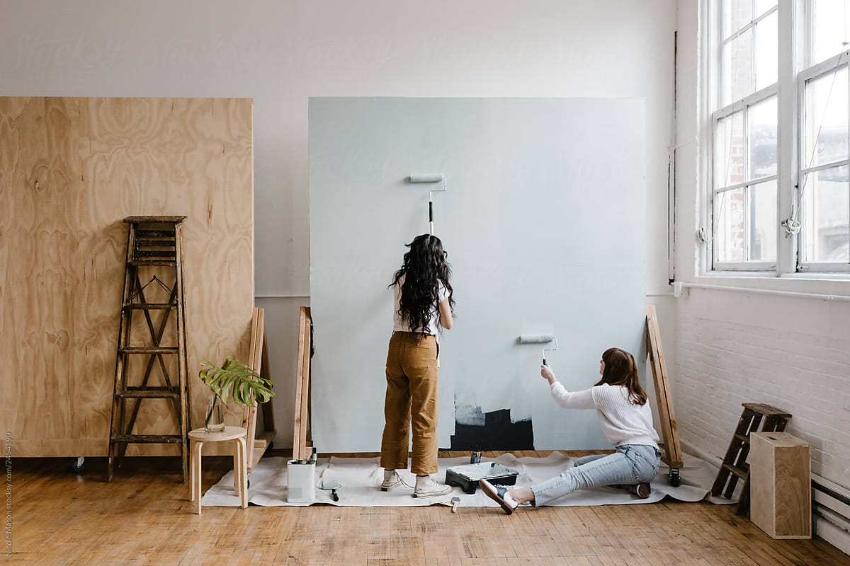 two women painting a backdrop in a modern bright industrial studio space