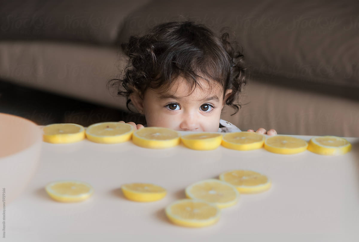 Playful Curious Toddler Peeking Over Table at Sliced Lemons.
