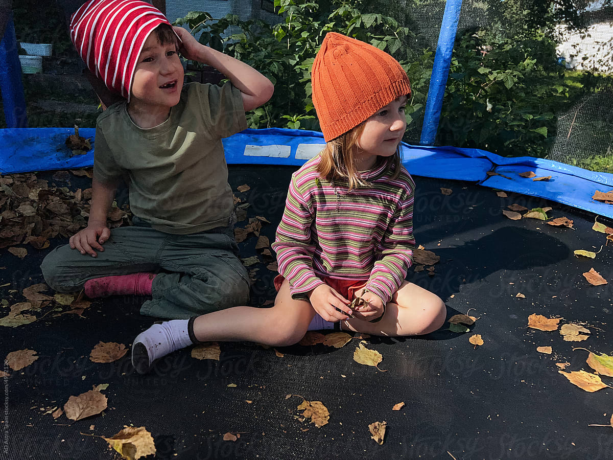 Two children sitting at the trampoline full of autumn leaves