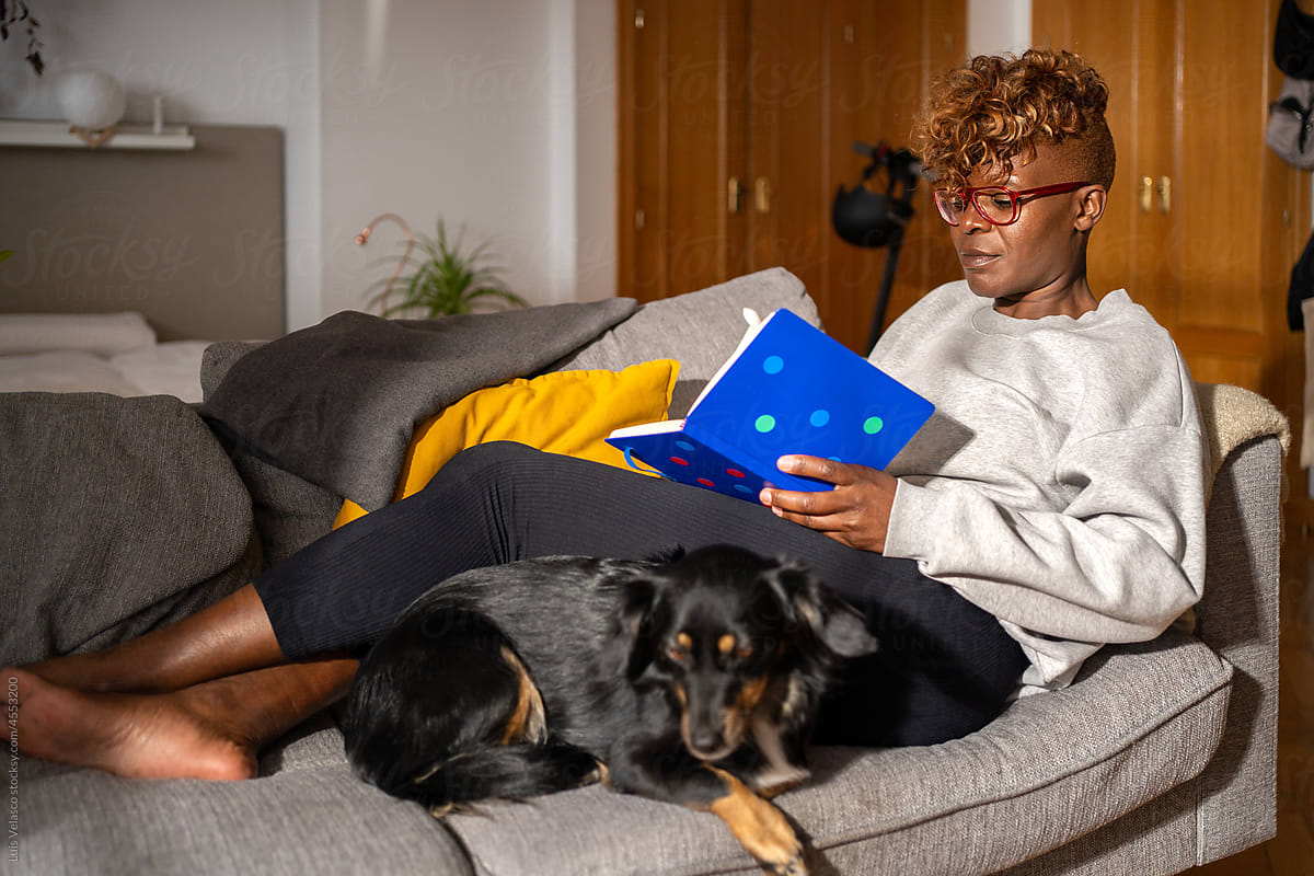 Black Woman Next To Her Dog Using A Blue Notebook On The Couch.