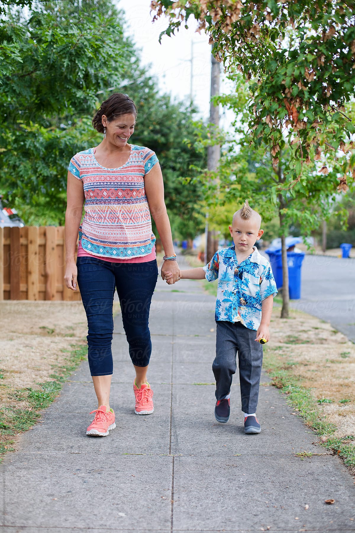 Mom and five year old boy holding hands walking on sidewalk