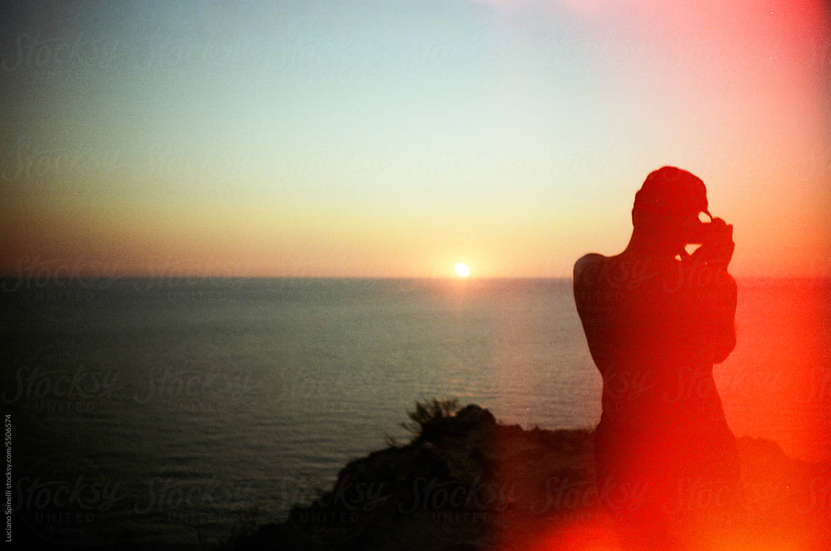 Silhouette of traveler taking picture of sunset - overexposed film