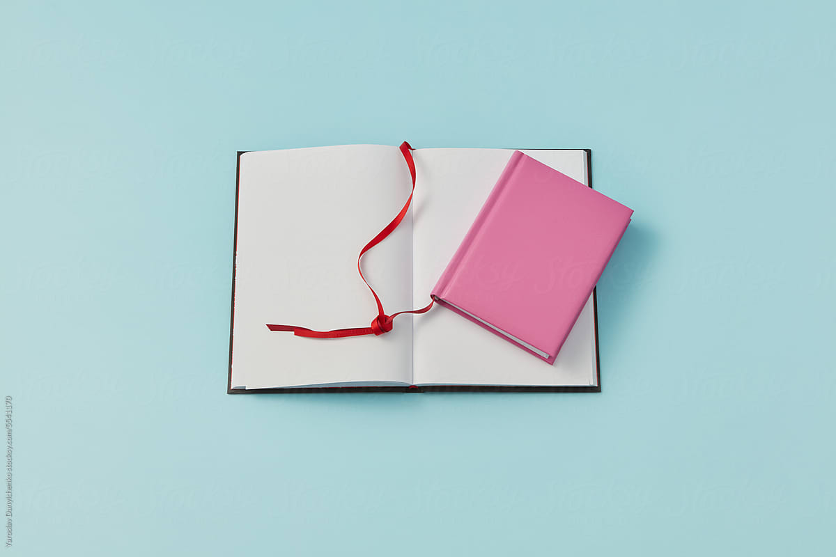 Pink book tied to open blank one by red bookmark.