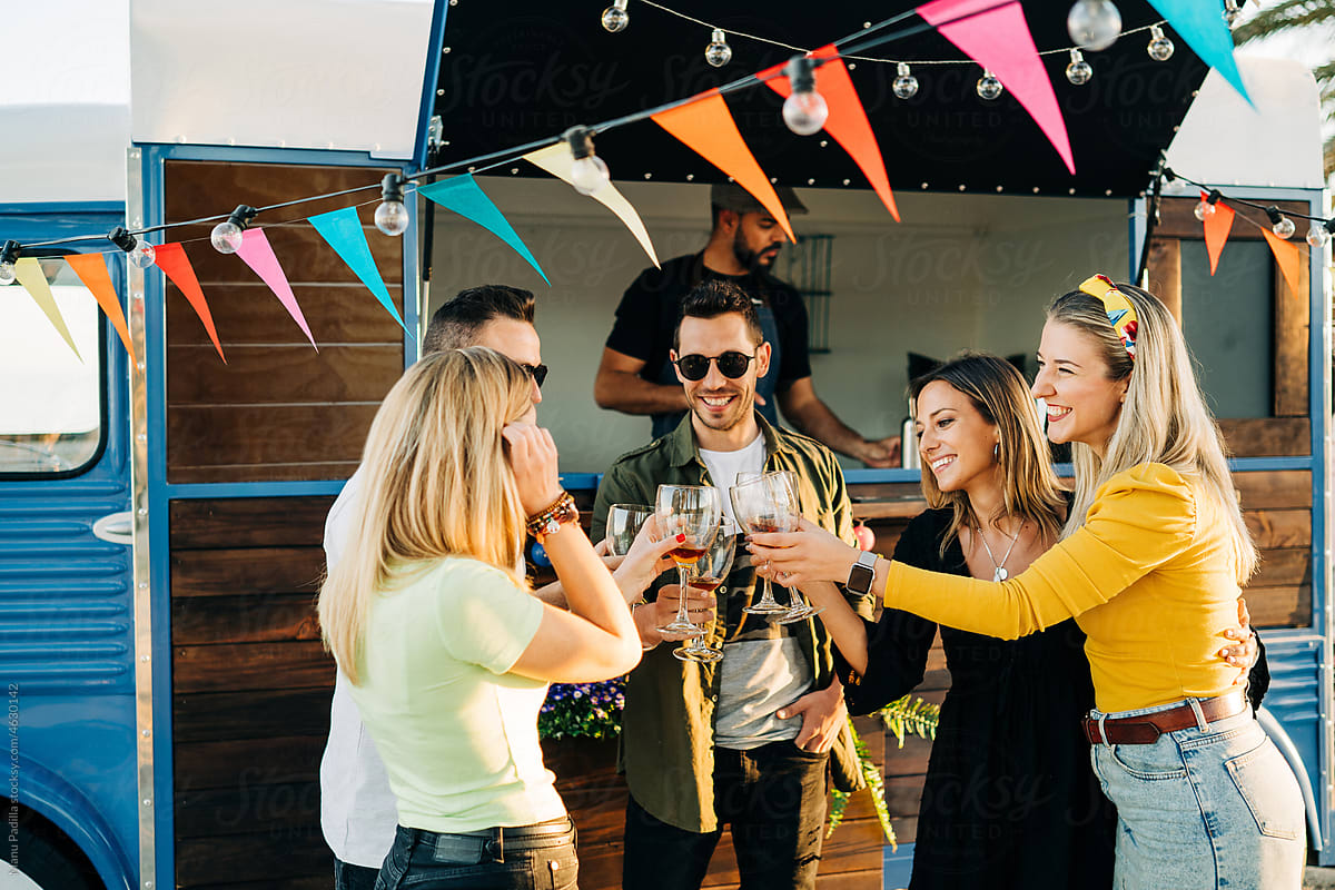 Group of happy friends clinking glasses near bar truck