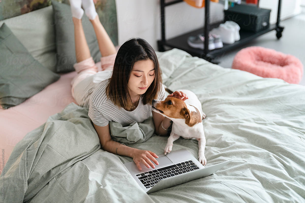 Happy woman lying with dog on bed