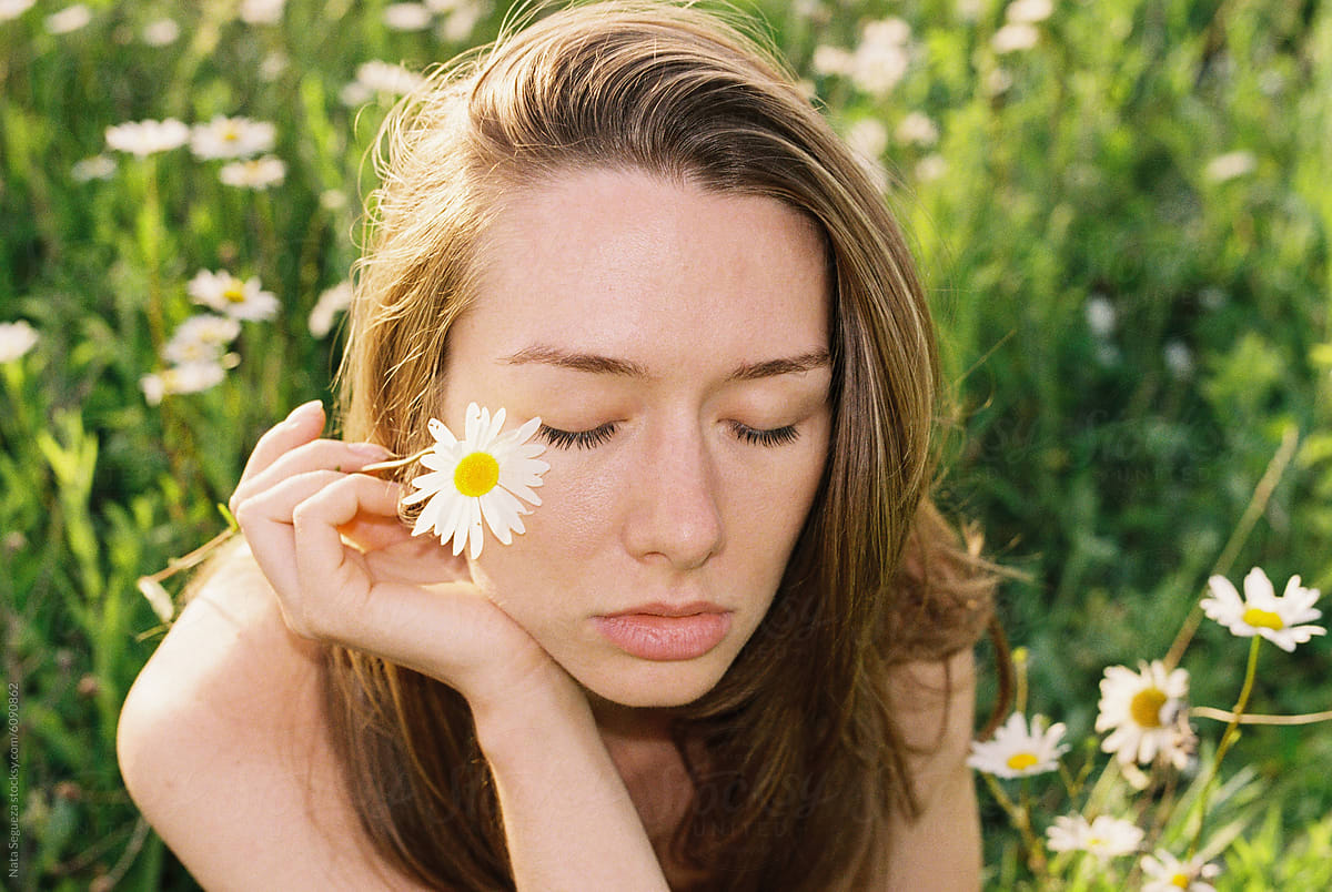 A woman holds a daisy in a sunlit field