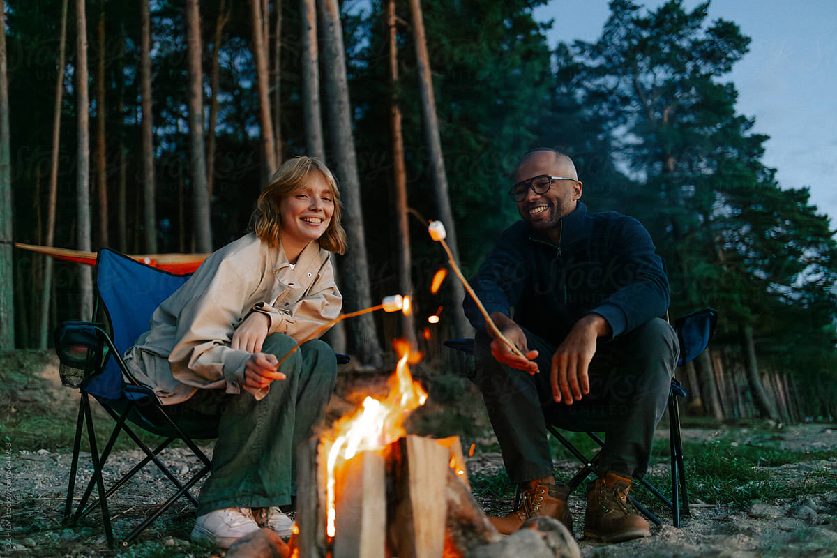 A man and a woman fry marshmallows in the woods