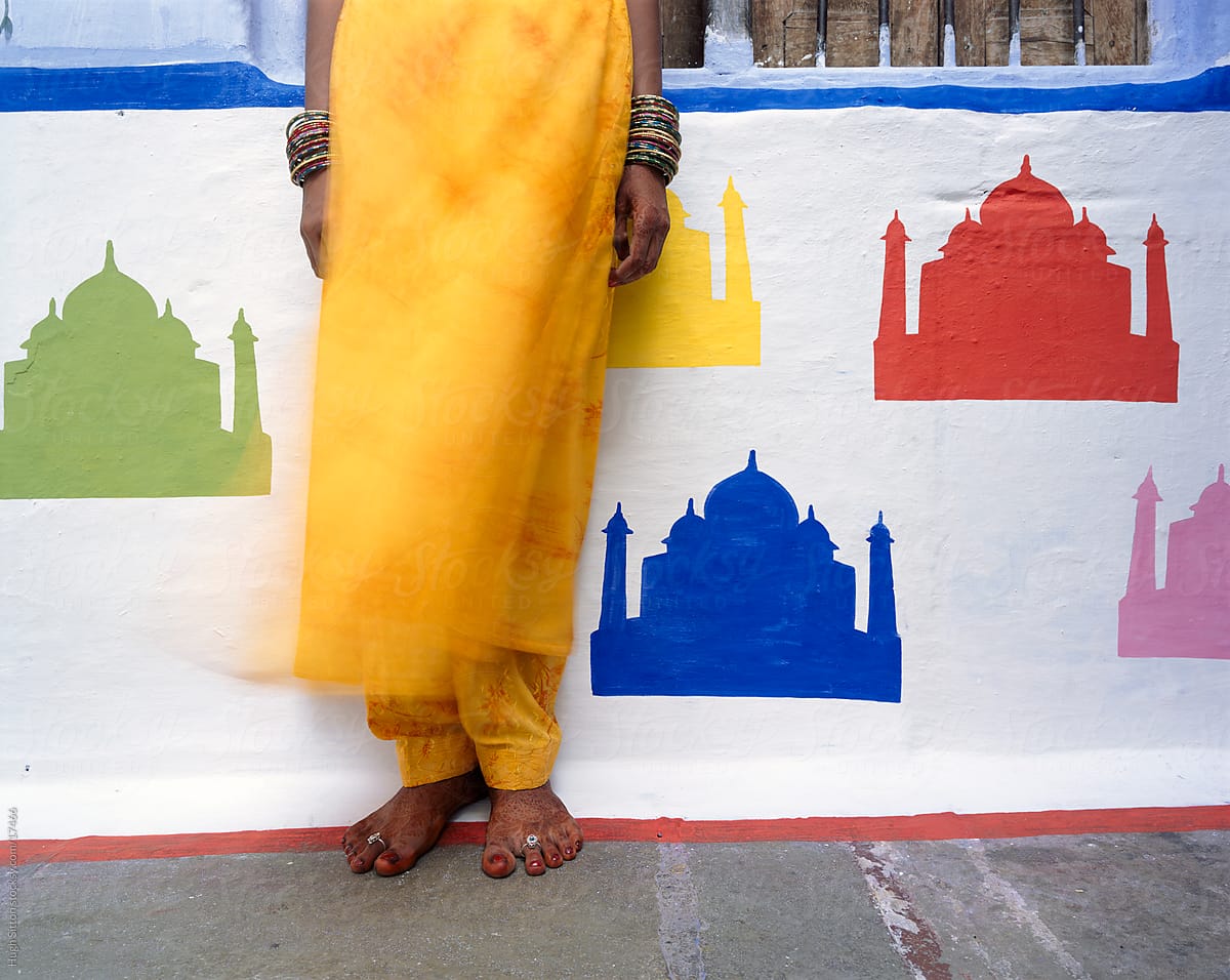 Indian woman standing infront of different coloured Taj Mahal\'s painted on wall.