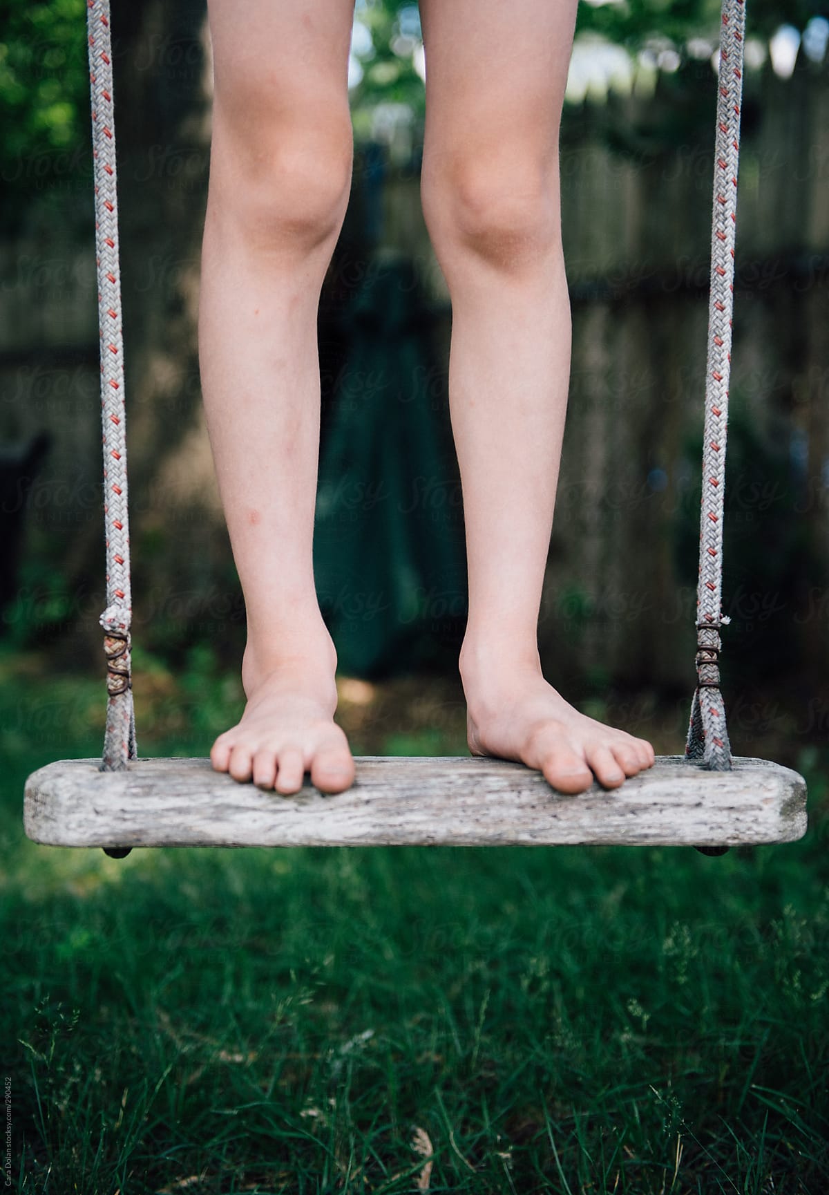 Child with bare feet stands on a wooden swing in his back yard