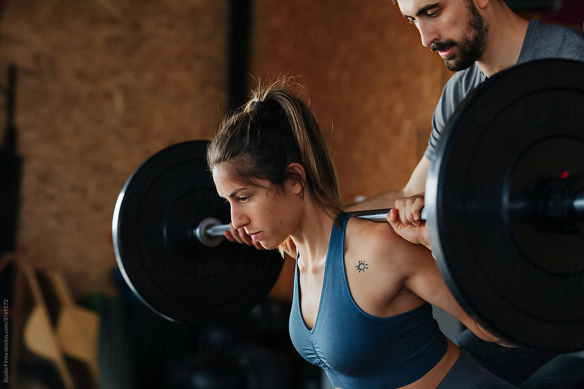 Man Helping Woman in Gym with Weightlifting