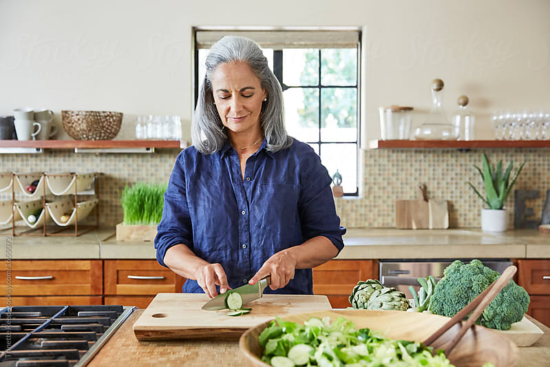 Portrait of mature woman cutting a cucumber for a healthy salad in the kitchen