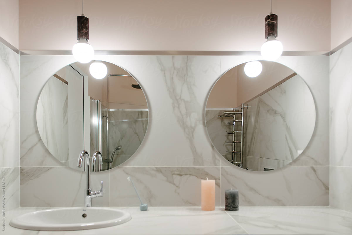 Pastel pink bathroom with two round mirrors and marble on the wall