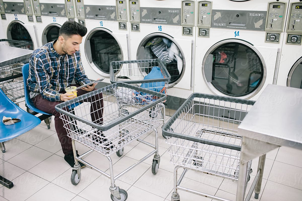 Young Man Reading e-Book in electronic tablet doing Laundry in L