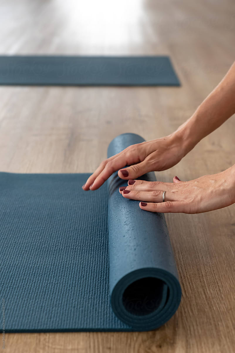 Woman rolling up yoga mat in modern studio