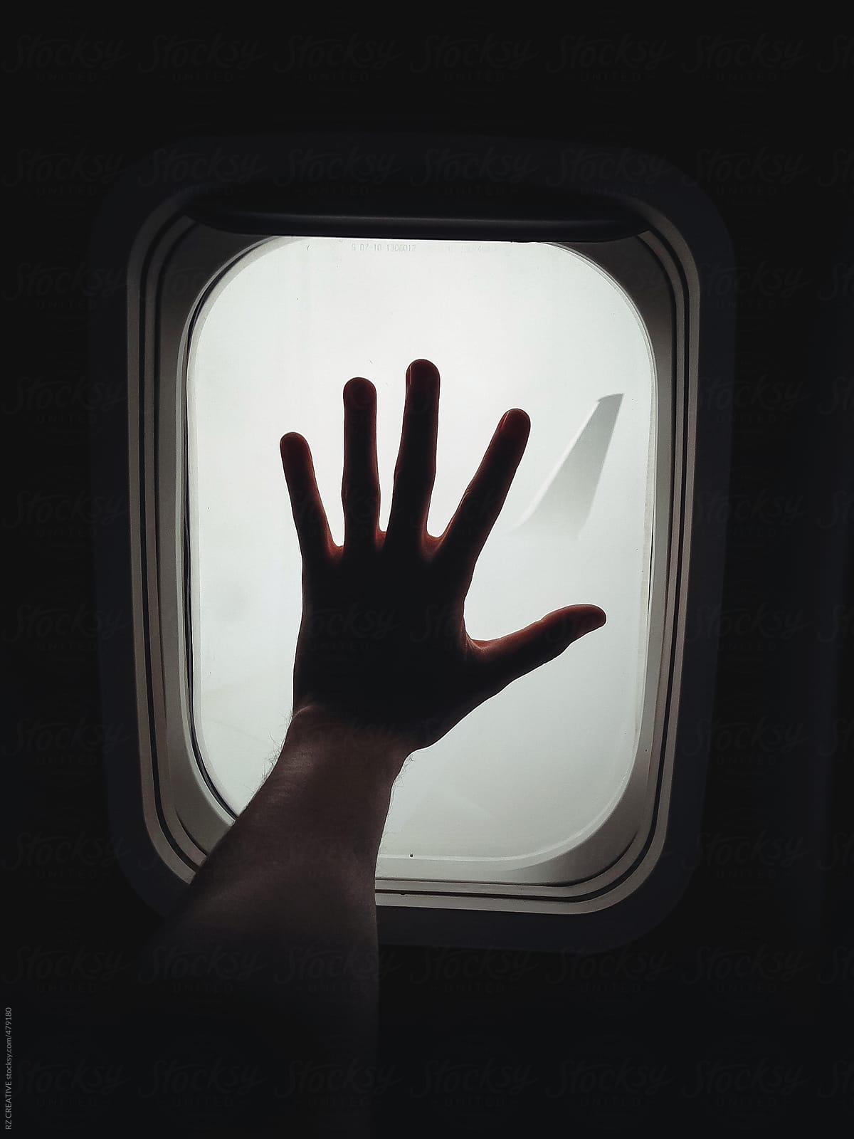 Hand against the window of a plane.
