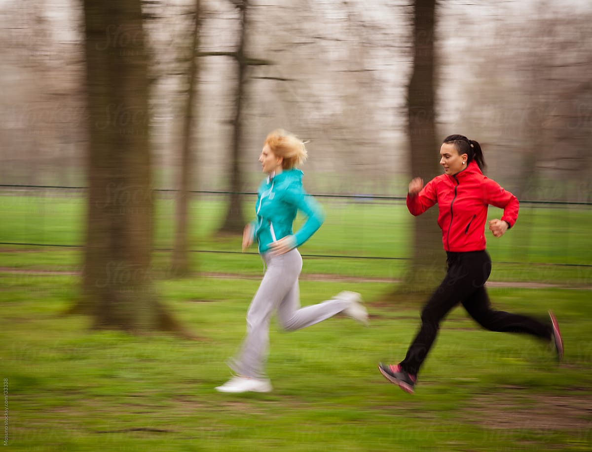 Two women jogging in the park on a rainy spring day.