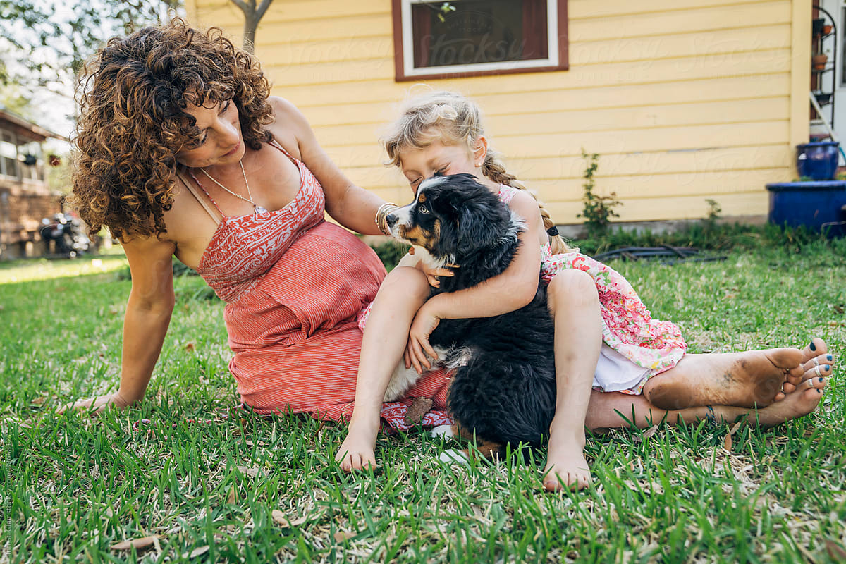 Girl sitting in mom\'s lap hugging puppy outside in yard