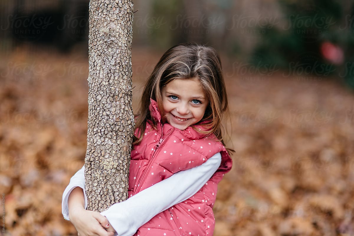 Cute Young Girl In A Vest Standing Outside Holding A Tree By Stocksy Contributor Jakob