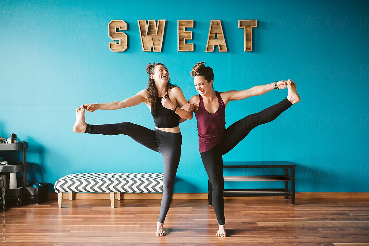Two friends holding a yoga pose in a fitness studio