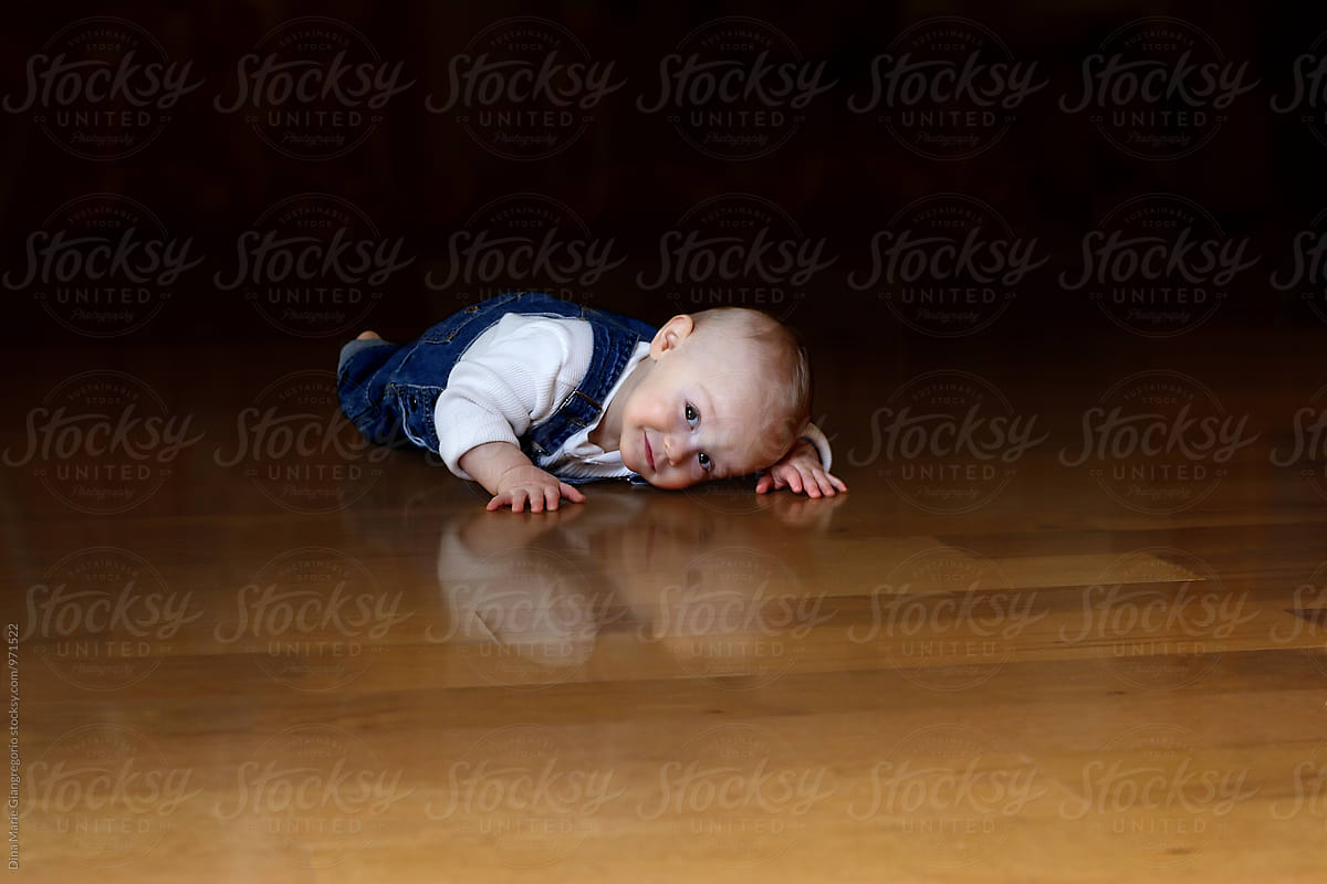 Baby in Denim Jumper Laying on Hardwood Floor.