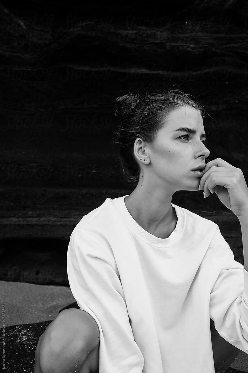 black and white portrait of a girl in profile, dressed in a white sweater on a background of mountains on the beach