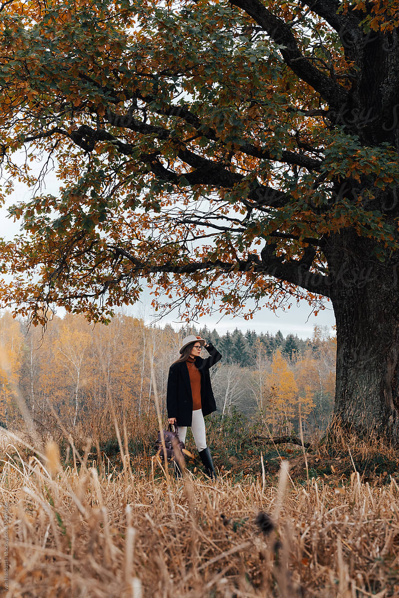 Stylish millennial woman in fall attire hikes through rustic field