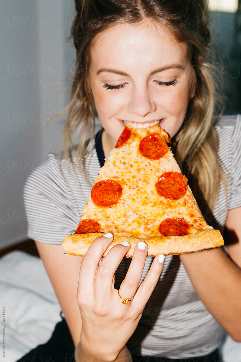 Young Woman Eating Slice Of Pepperoni Pizza On Bed In Apartment By Stocksy Contributor Jesse 