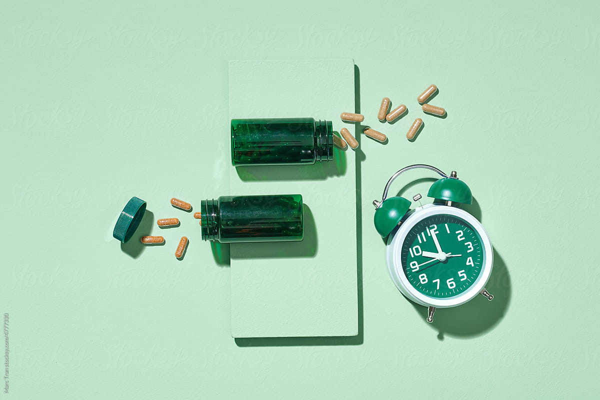 Pile pills, green bottles and green alarm clock on green
