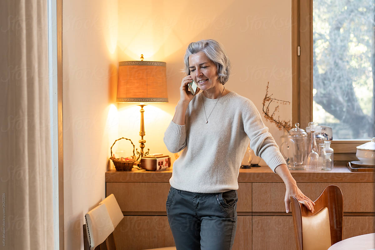 Mature female speaking on smartphone at home