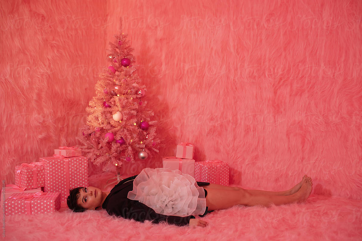 Stylish young woman laying under pink Christmas tree