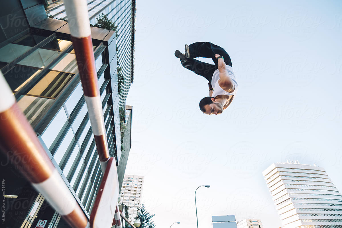 man doing a backflip in the air over a barrier during a parkour training in a city