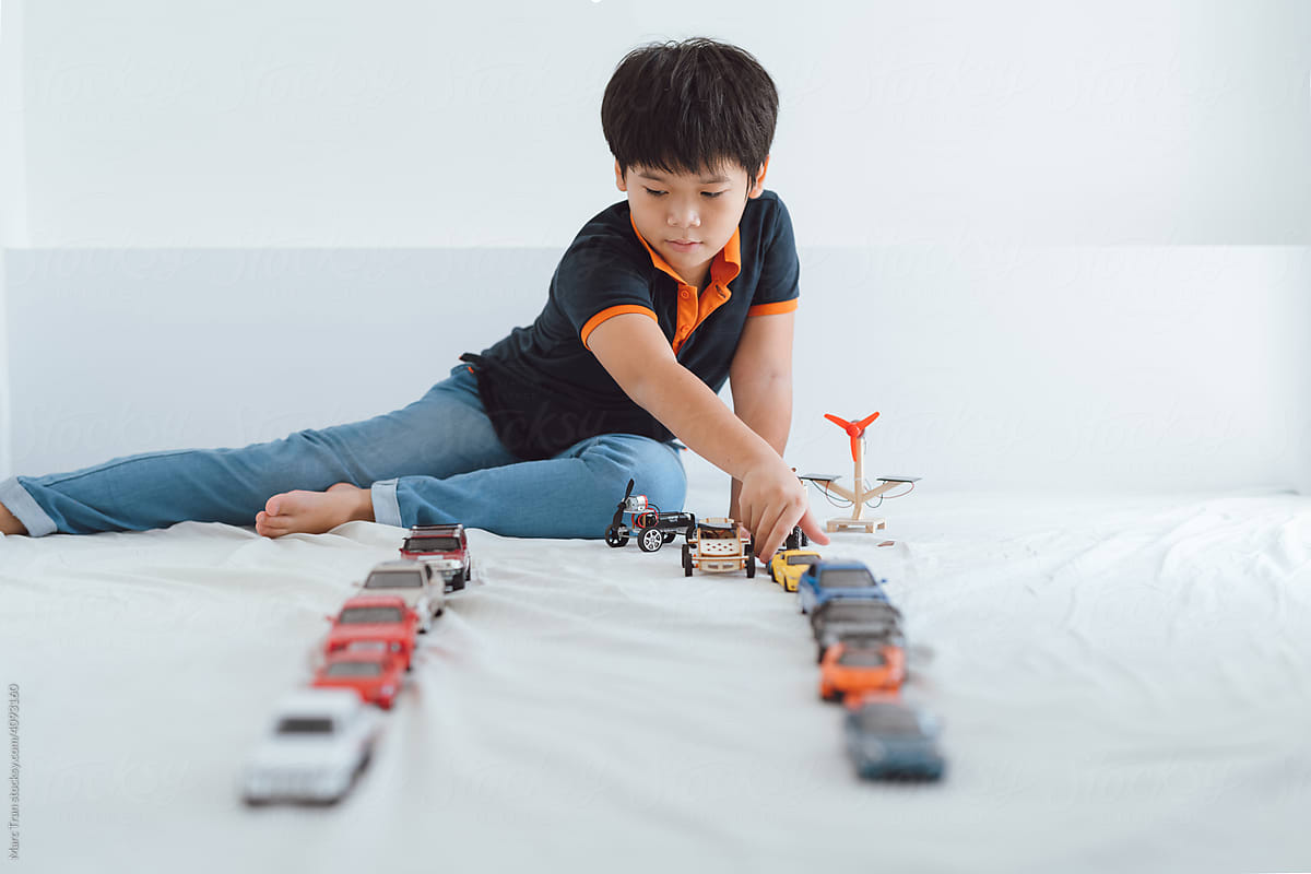 a schoolboy lying on the floor playing with toy cars
