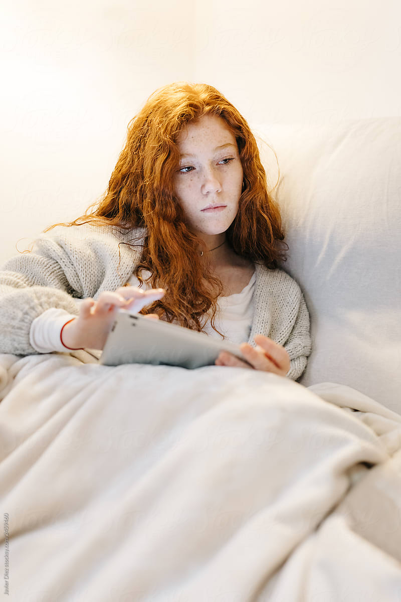 Pensive woman with tablet on bed
