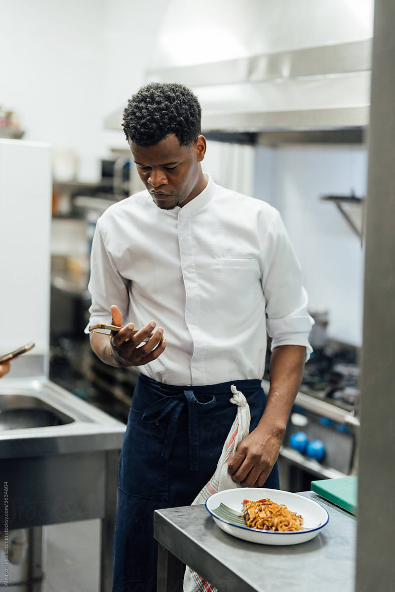 Black chef using smartphone in kitchen in restaurant