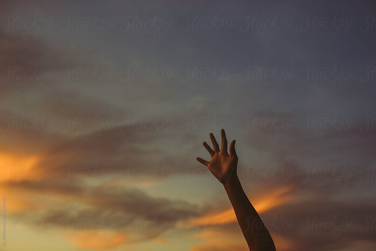 Hand reaching for the clouds at sunset.