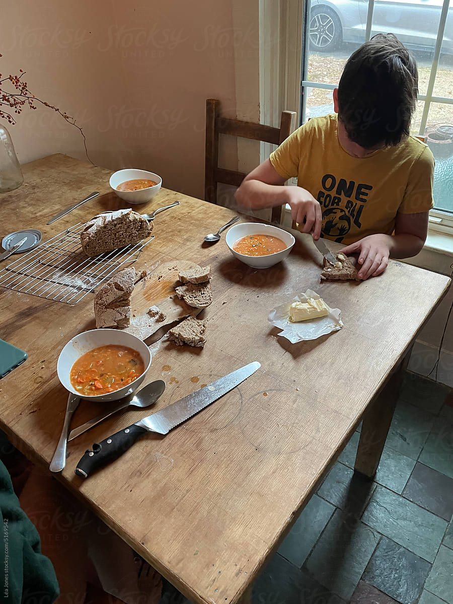 boy buttering homemade bread next to bowl of soup