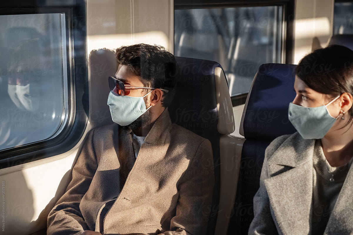 Male and female passengers in masks looking out train window