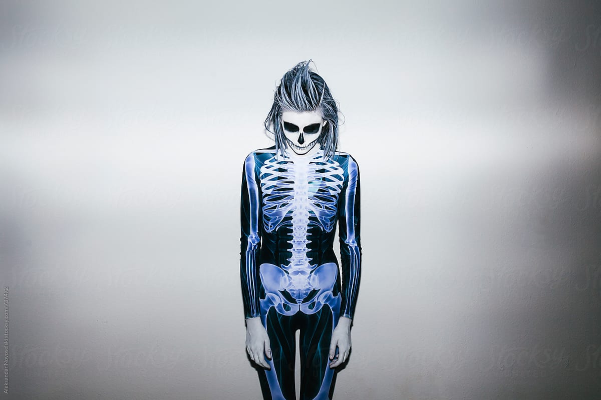 Young woman with skeleton costume and halloween make up against white wall