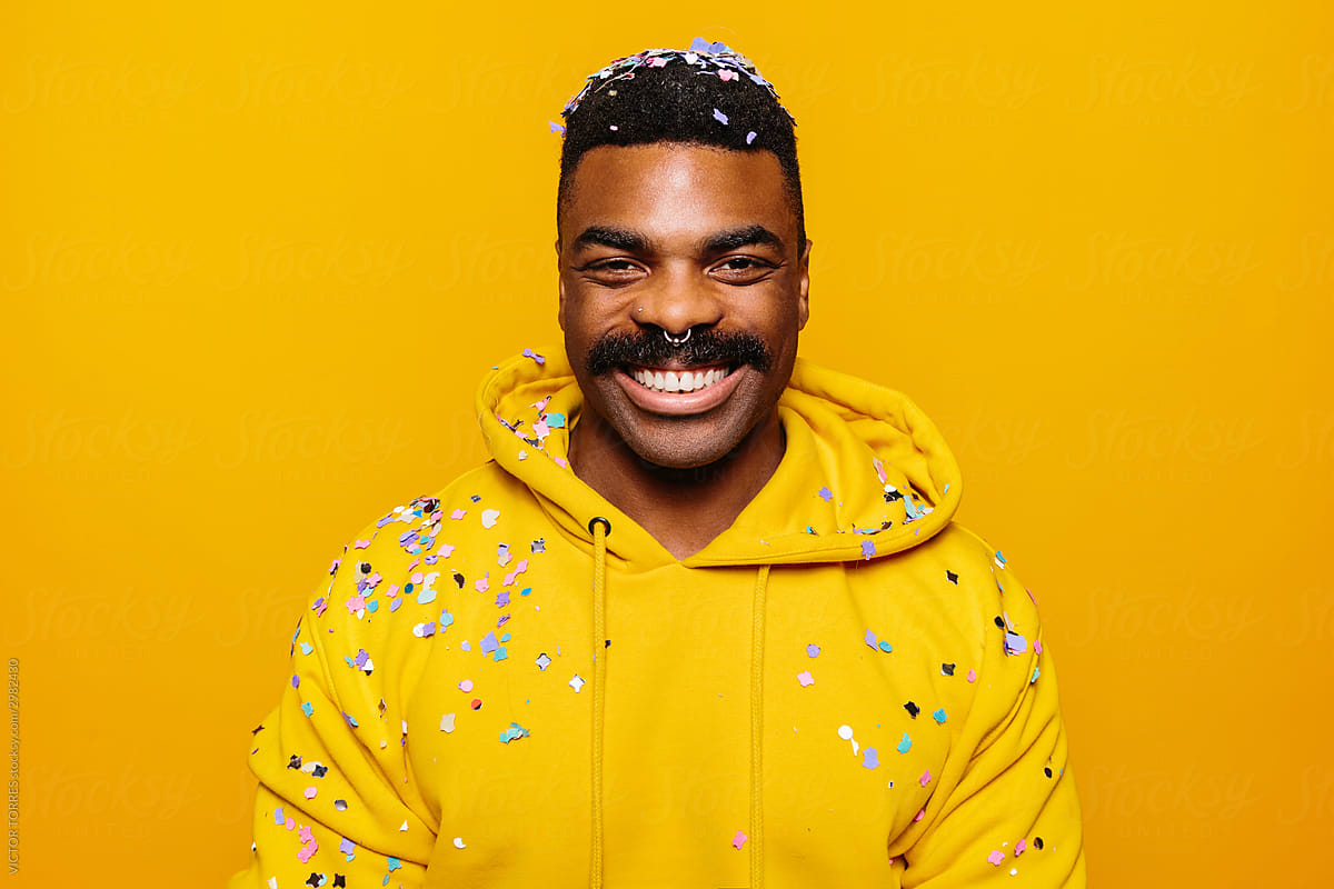 Happy african american man over yellow background with confetti on head