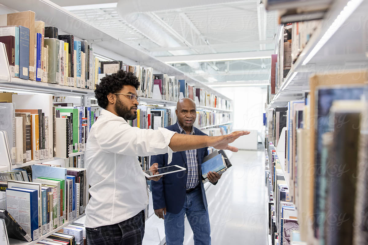 Librarian helping man find book in library.