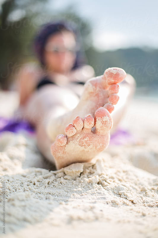 Woman\'s feet on the white sand near the sea