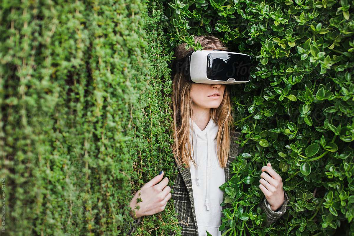 Blond girl in VR headset trapped in a green hedge
