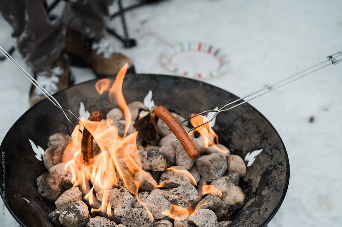 Hot dogs grilled over a portable fire pit in the snow.