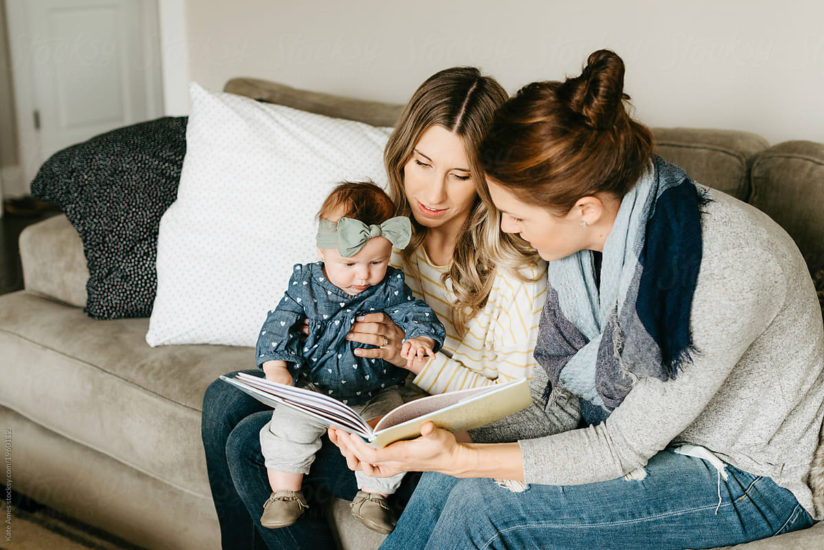 Lesbian Moms Reading To Their Young Daughter In Their Living Room Del Colaborador De Stocksy
