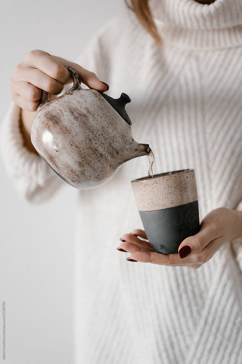 Crop woman pouring tea in rustic mug