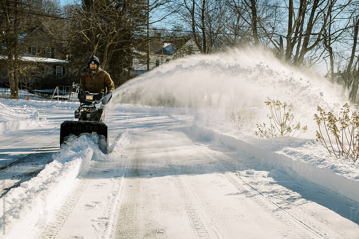 millennial man snow blowing his property after snow storm
